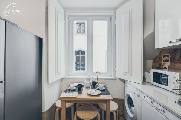 A compact kitchen with a window, a washing machine, and a microwave.