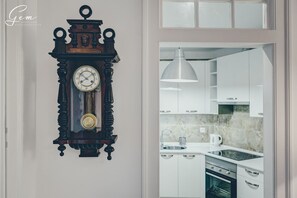 A wall-mounted antique clock with a pendulum, a modern kitchen with white cabinets, a stainless steel sink, and a pendant light.