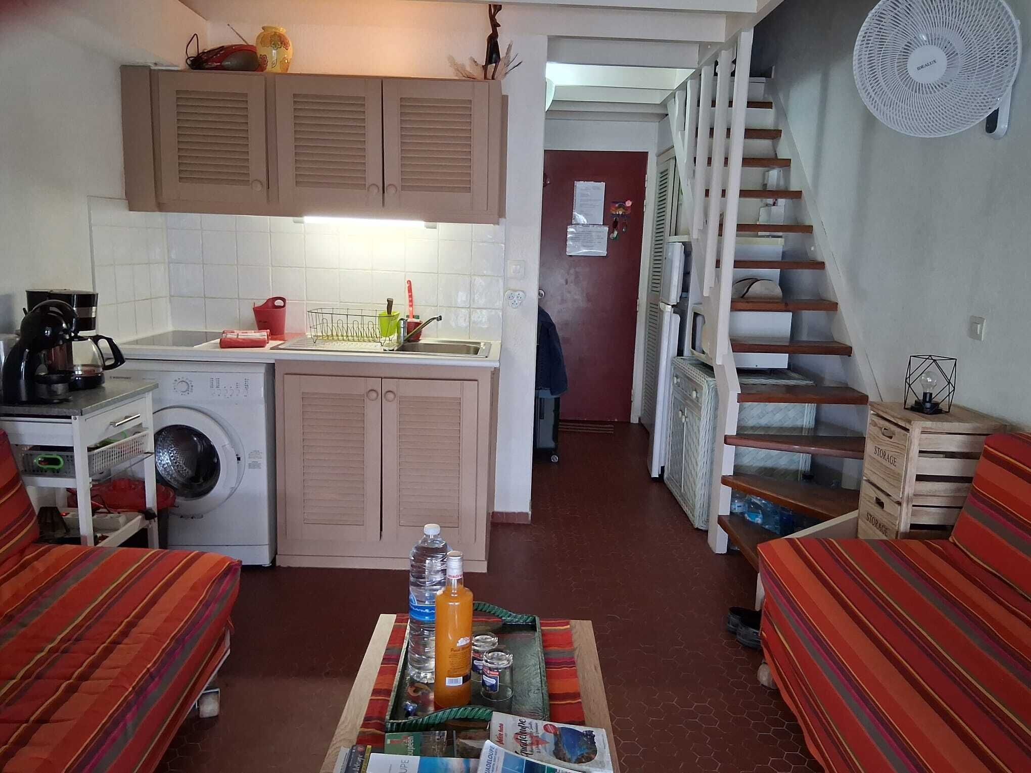 Una cuina compacta amb rentadora, cafetera i zona de menjador amb taula per a dues persones.