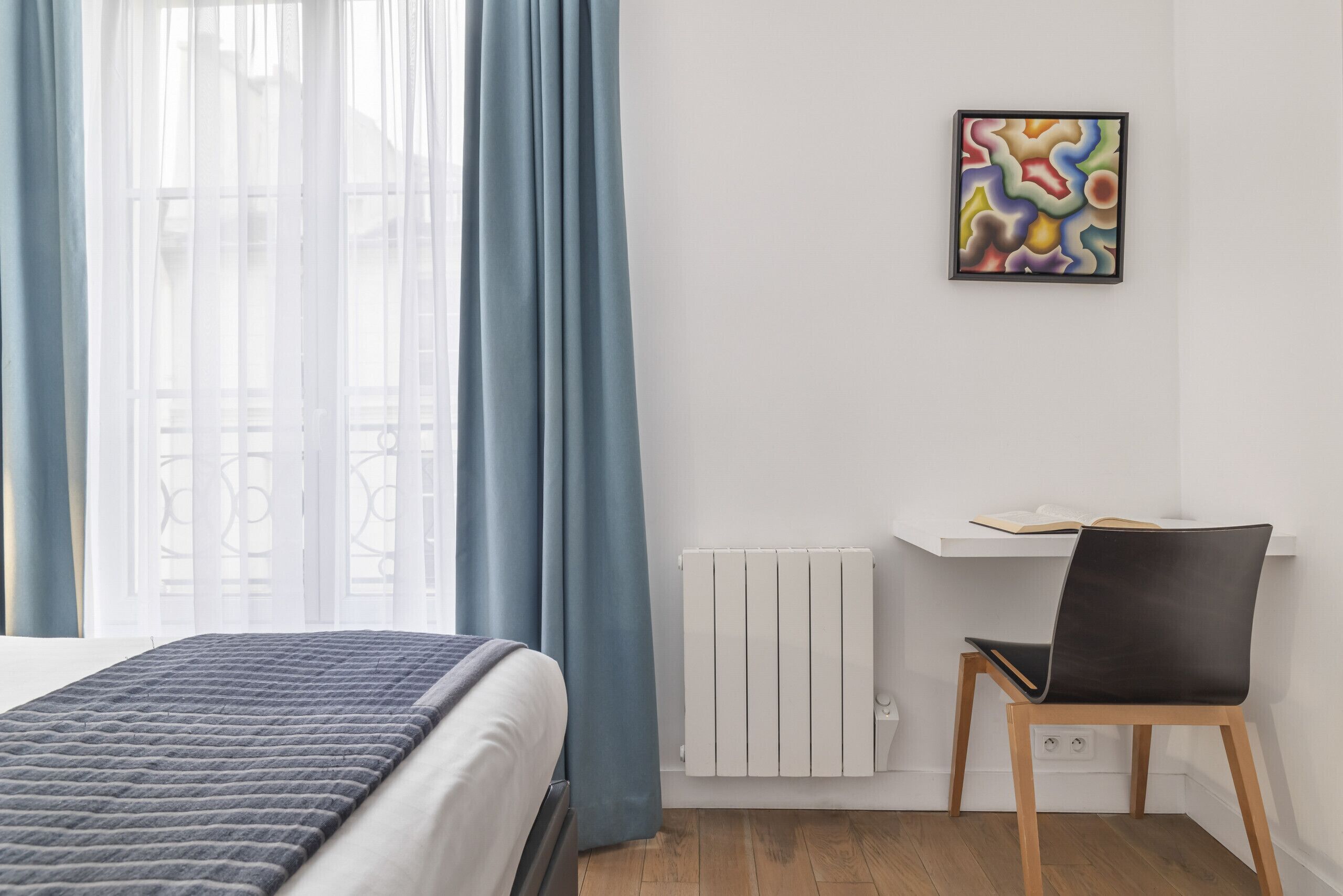 A modern bedroom with a bed, a chair, a radiator, and a wall-mounted artwork.