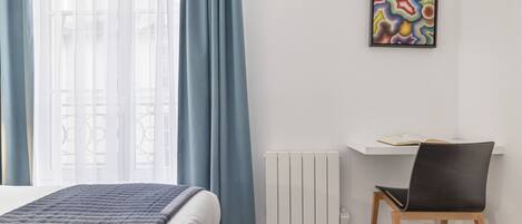 A modern bedroom with a bed, a chair, a radiator, and a wall-mounted artwork.