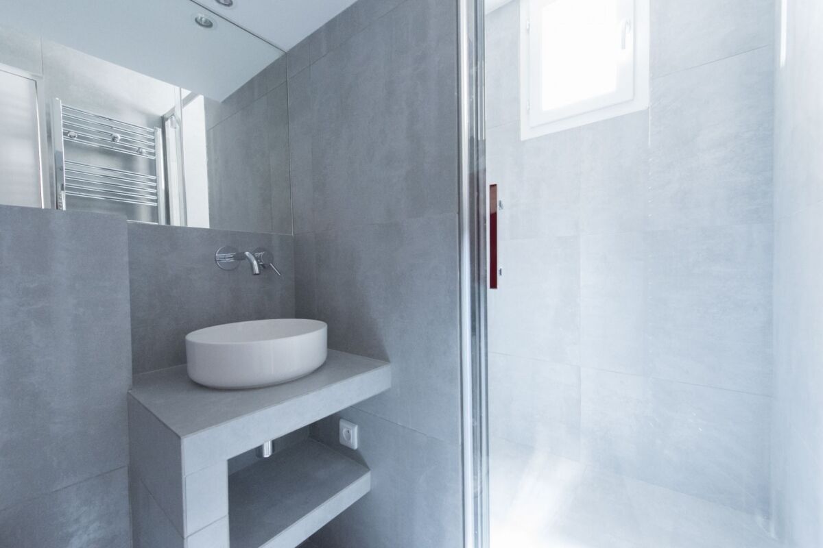 Une salle de bain moderne avec un lavabo blanc, un porte-serviettes et une cabine de douche en verre.