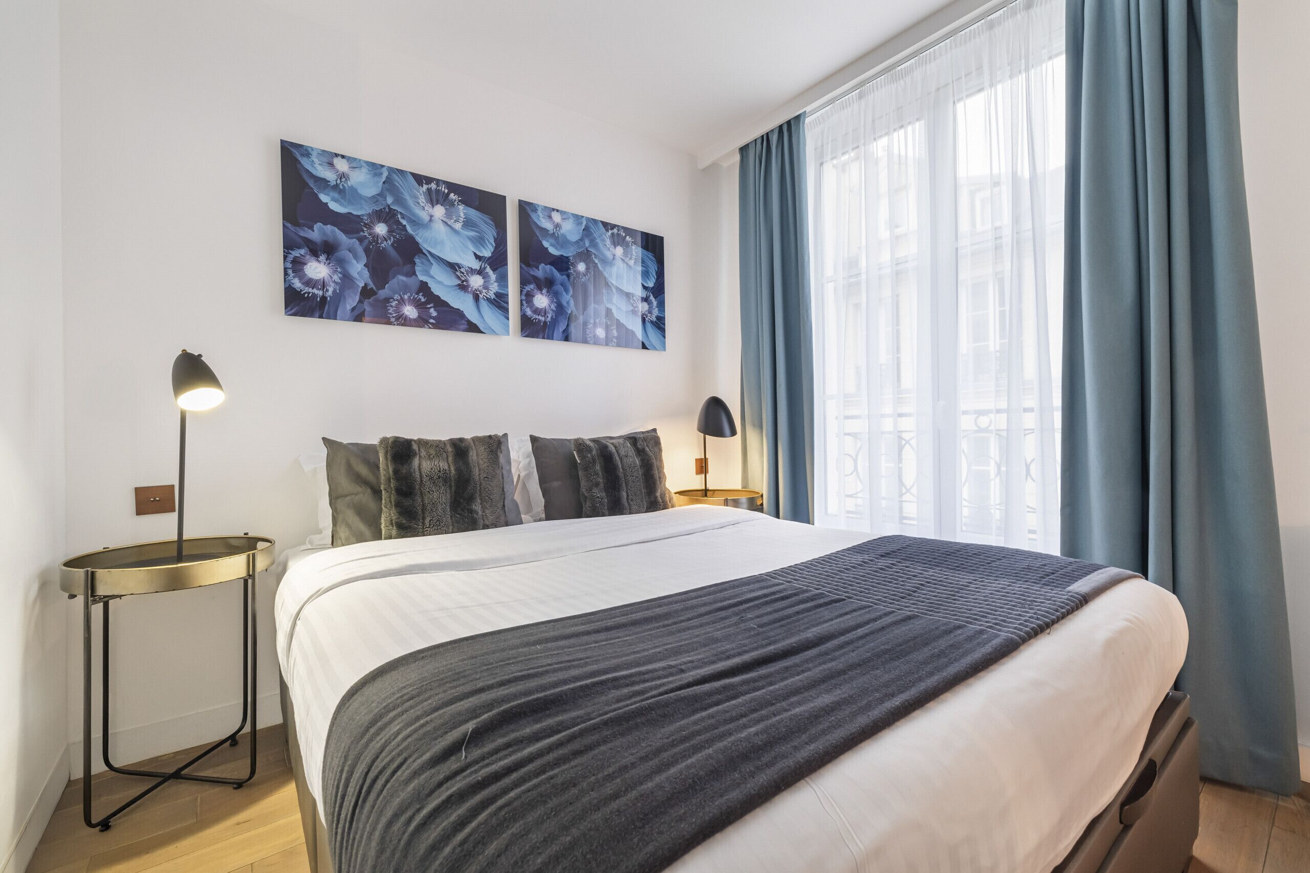 A modern hotel room with a large bed, two wall-mounted lamps, and a window with blue curtains.