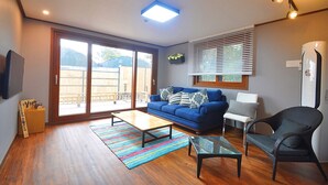 A living room with a blue sofa, a glass coffee table, a wicker chair, and a sliding glass door leading to a patio. - NonilSO Private Pension (Seogwipo)