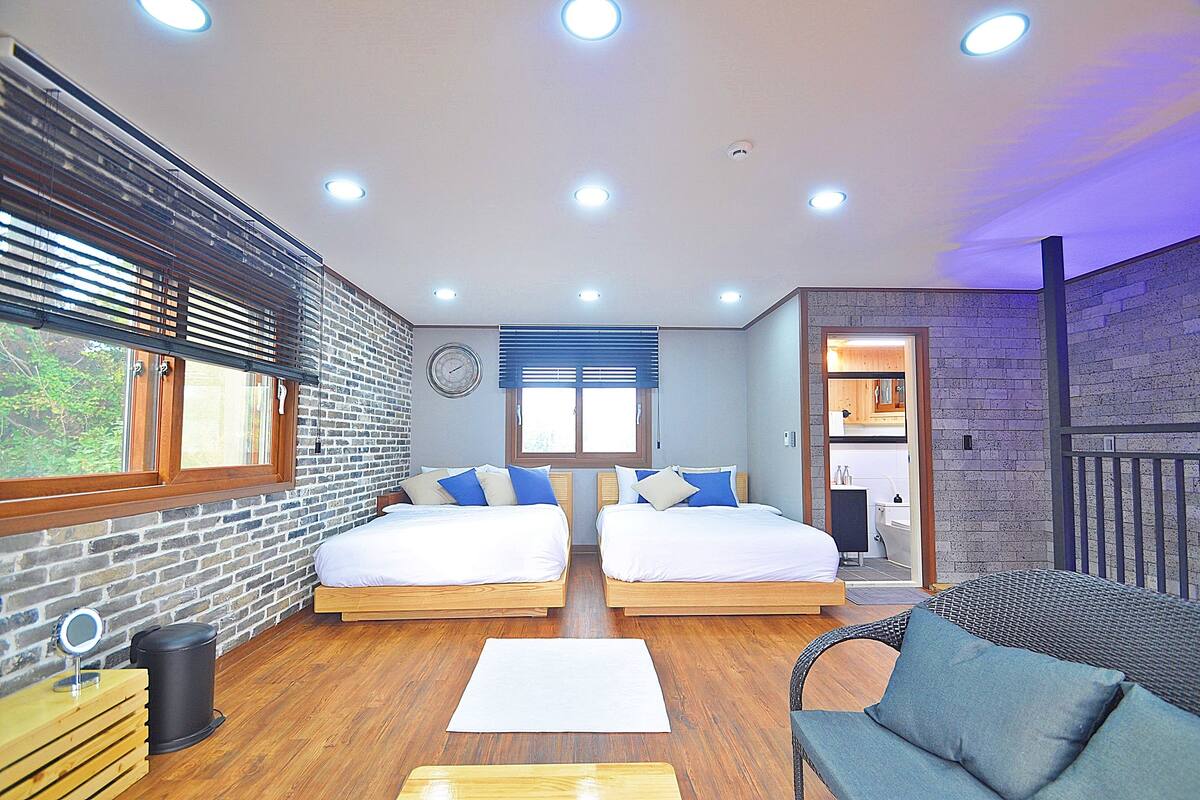 A modern room with two beds, a sofa, a small table, and a window with blinds.