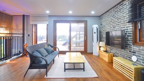 A modern living room with a sofa, a coffee table, and a TV on a brick wall. - NonilSO Private Pension (Seogwipo)