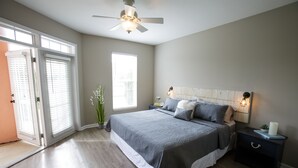 Une chambre avec un grand lit, une table de chevet, un ventilateur de plafond et une vue sur l’extérieur grâce à une porte coulissante.