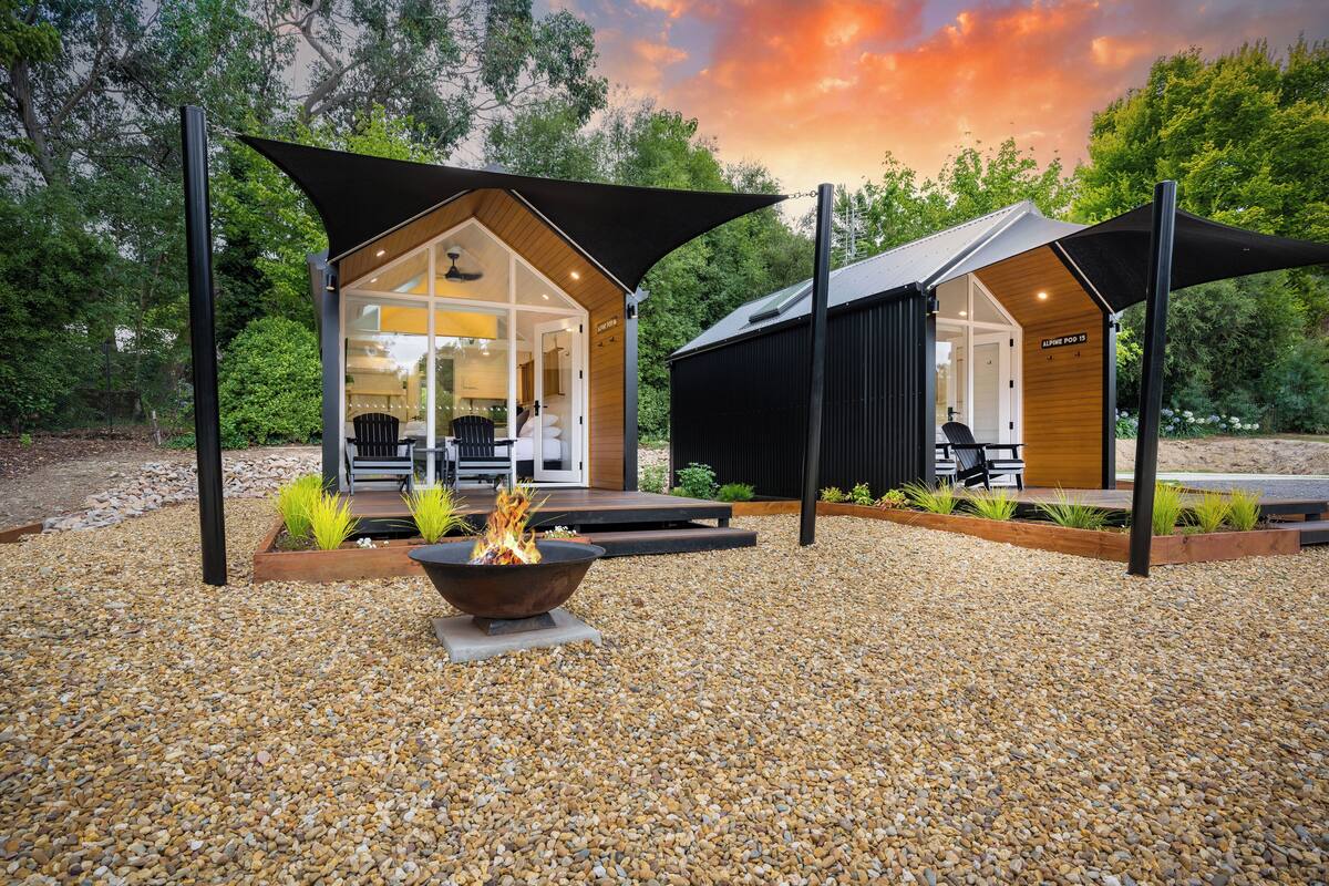 A modern outdoor seating area with a fire pit, surrounded by a gravel patio and shaded by large canopies.