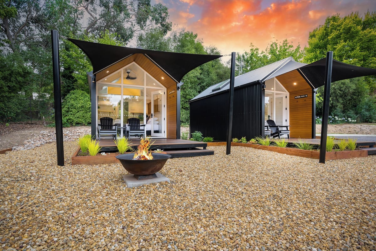 A modern outdoor seating area with a fire pit, surrounded by a gravel patio and shaded by large canopies.