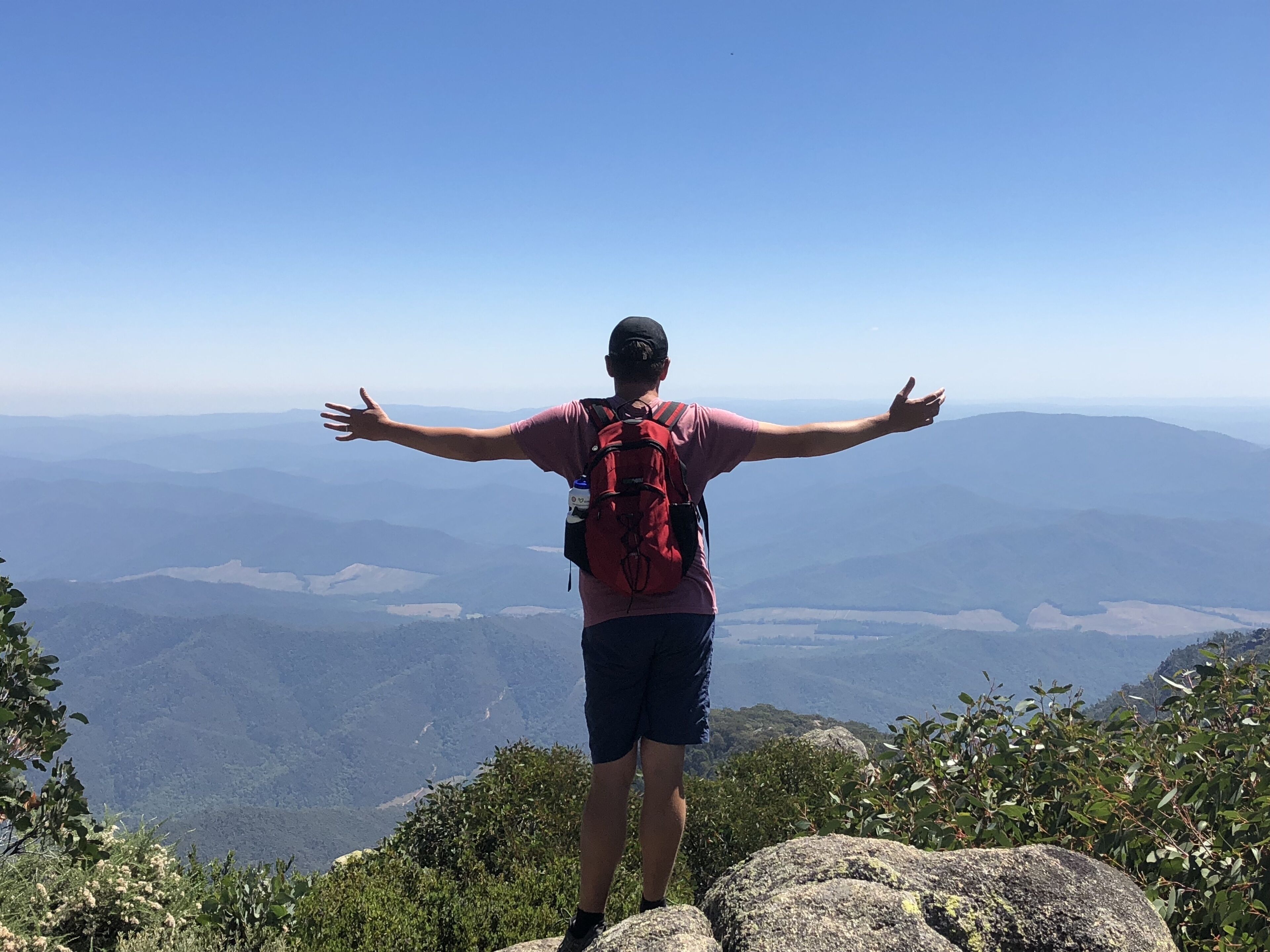 Una persona parada sobre un afloramiento rocoso, con los brazos extendidos, contemplando un paisaje montañoso.