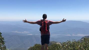 Una persona parada sobre un afloramiento rocoso, con los brazos extendidos, contemplando un paisaje montañoso.