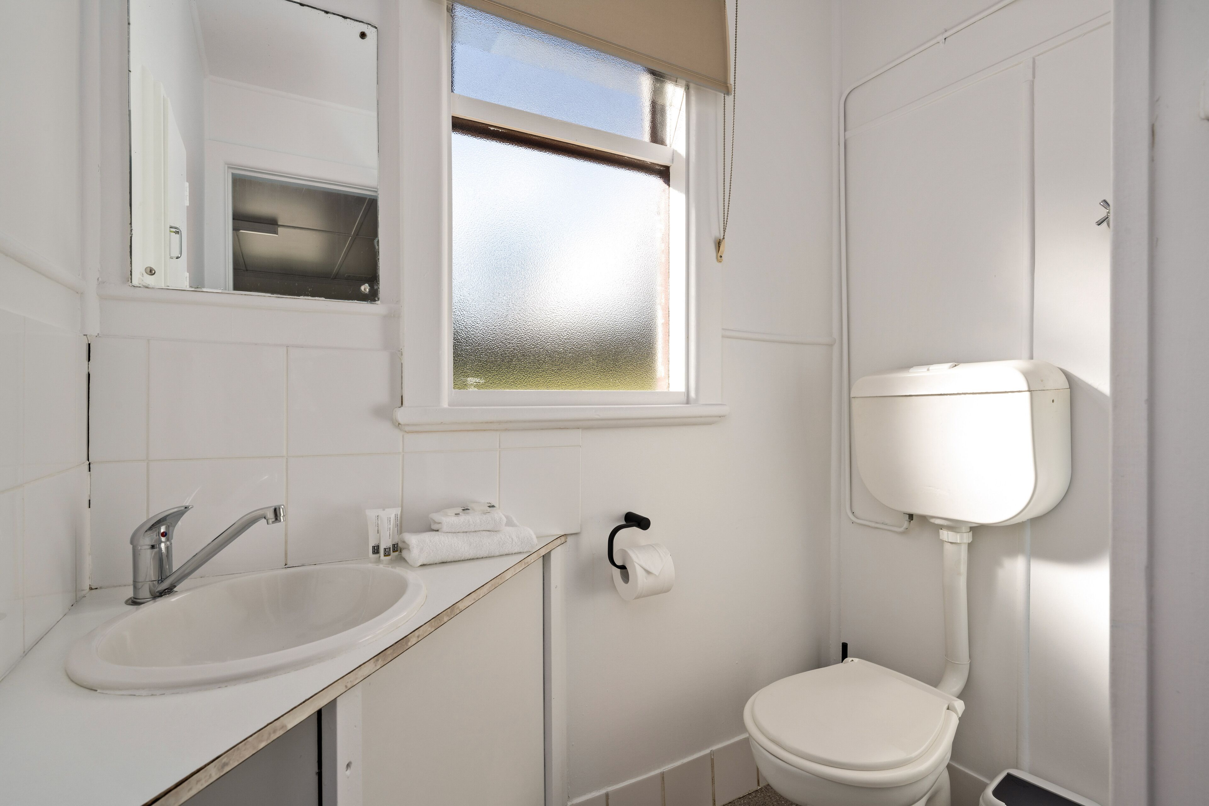 A small, clean bathroom with a white sink, a toilet, and a window.