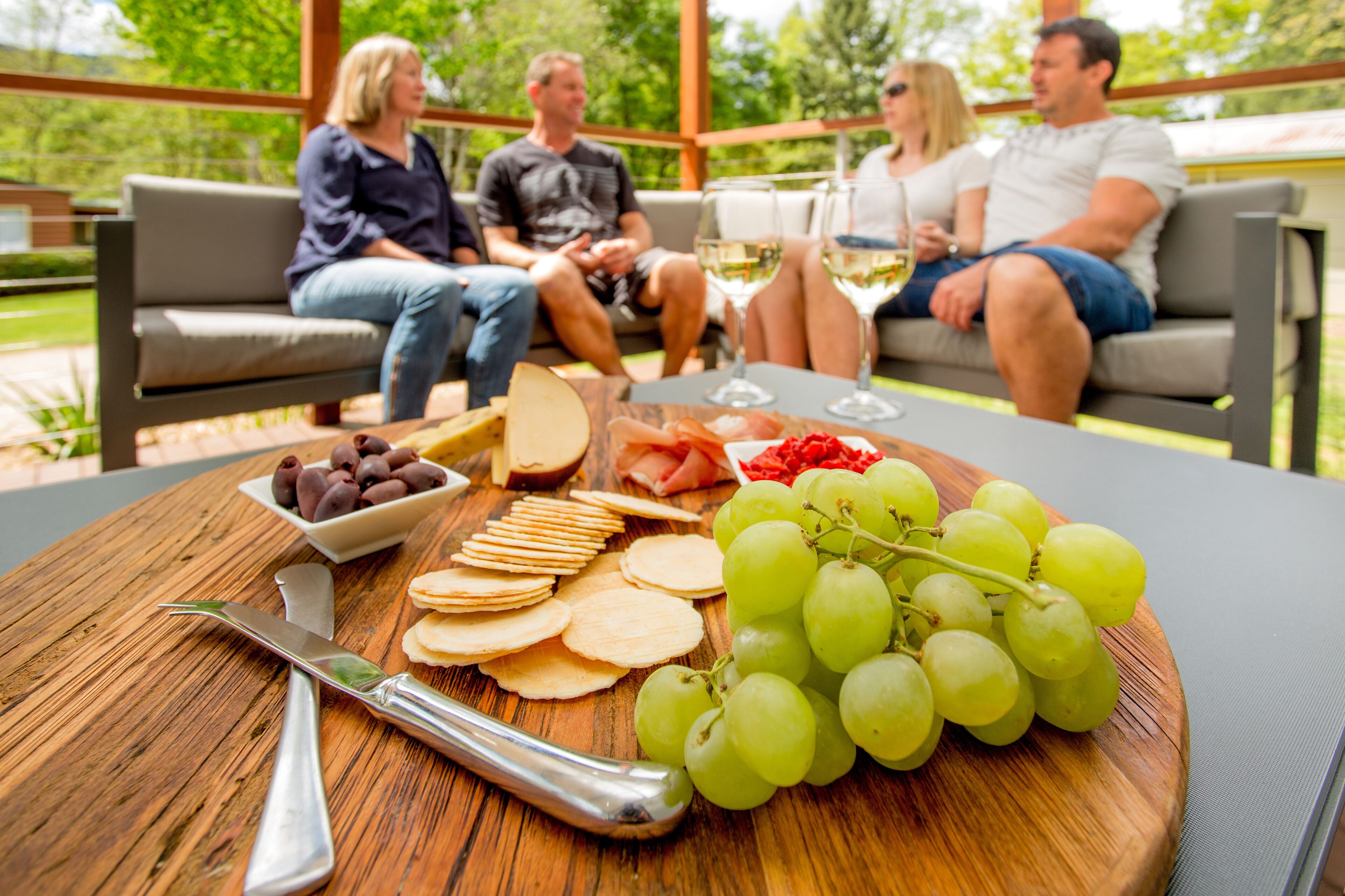 A wooden table with a cheese board, grapes, crackers, and a knife.