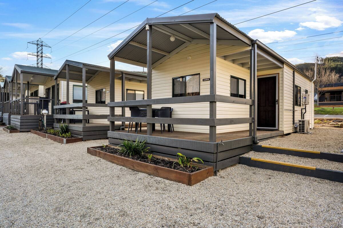 A row of cabins with a covered porch, wooden deck, and a gravel ground.