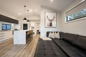 Una cocina moderna con una isla central, un comedor con taburetes de bar, una sala de estar con sofá de cuero y una gran obra de arte de un ciervo enmarcado en la pared.