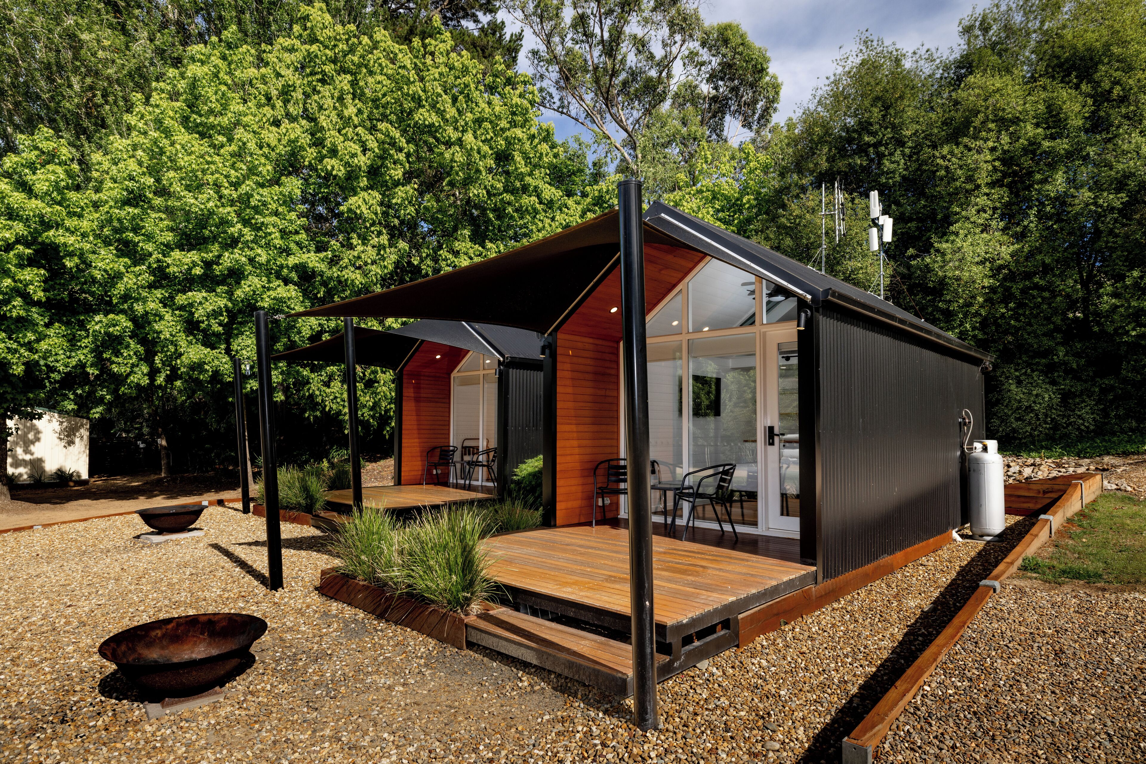 A modern cabin with a wooden deck, a covered patio, and a glass door leading to an interior space with seating.