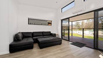 Uma sala de estar moderna com um sofá seccional, uma grande porta de vidro deslizante que dá para um deck externo e um ar-condicionado embutido na parede.