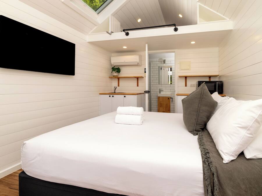 Un dormitorio moderno con cama, almohadas, televisión de pantalla plana y tragaluz.