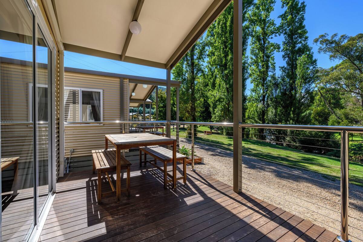 A wooden deck with a table and benches, overlooking a grassy area with trees.