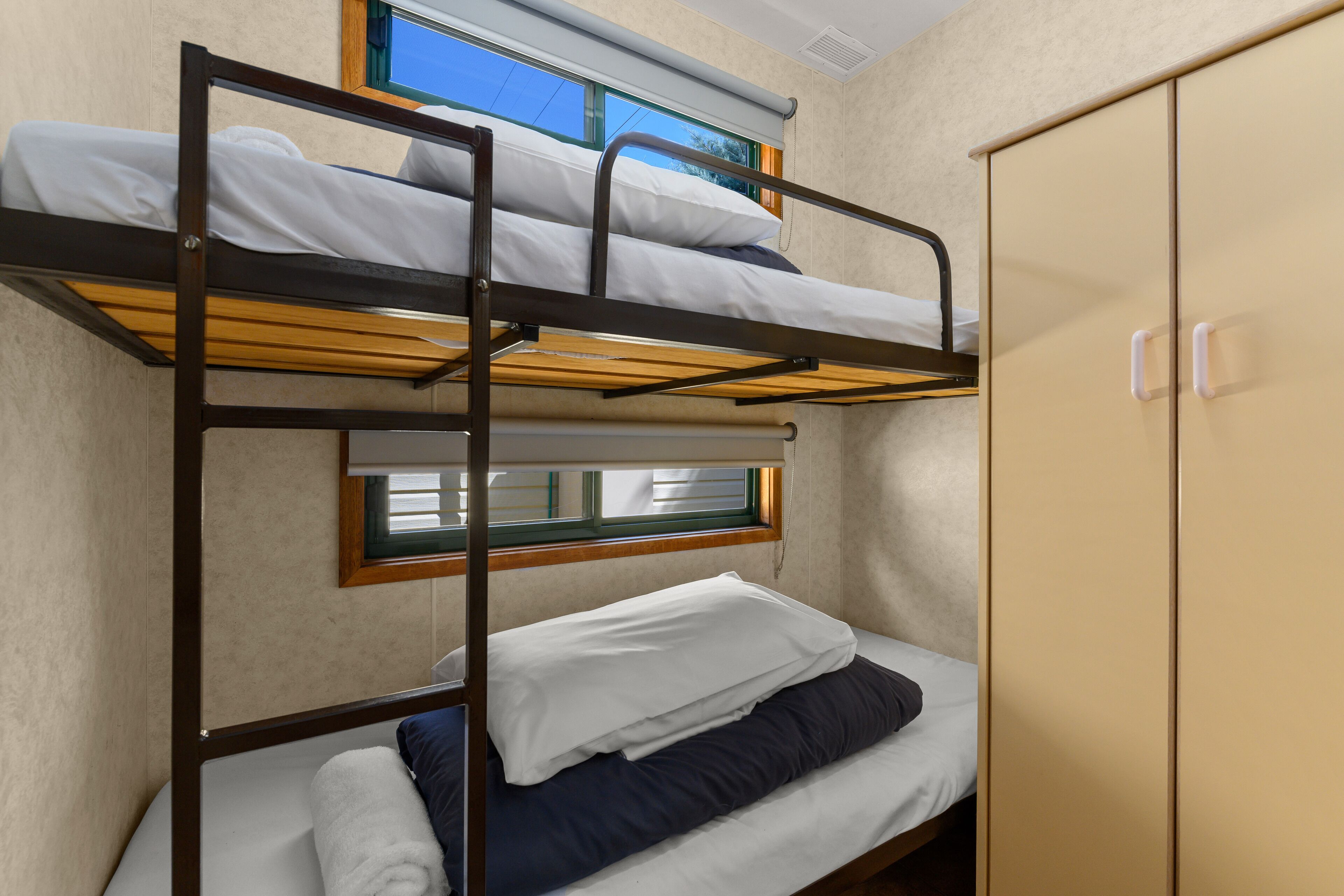 Una cama literera con ventana, un armario y una mesita.