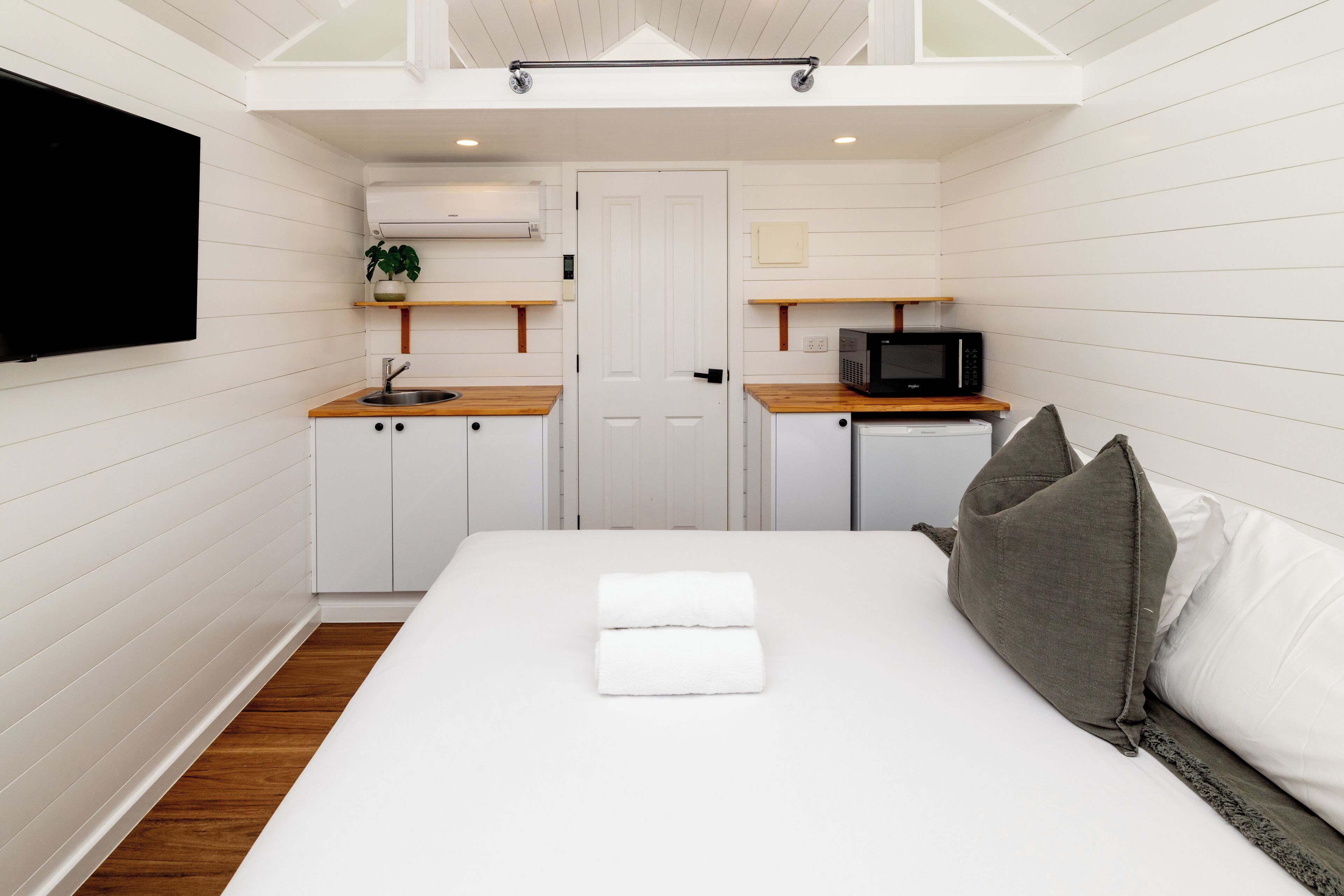 A compact hotel room with a bed, a small kitchenette, and a television.