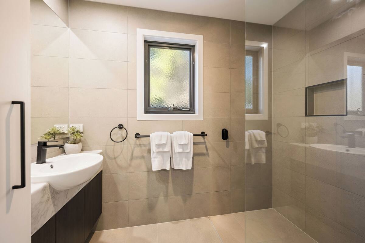 A modern bathroom with a large sink, a window, and a glass shower enclosure.