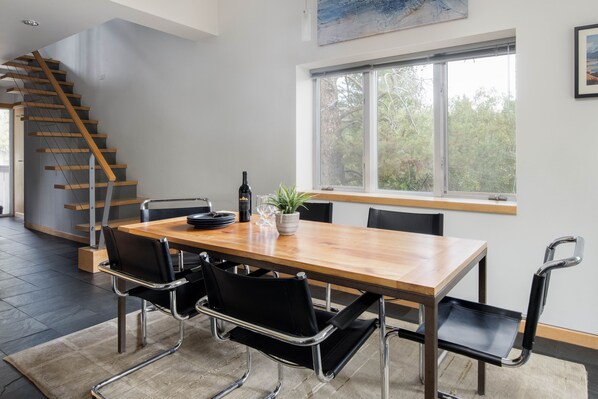 A modern dining area with a wooden table, black chairs, and a staircase. - Outpost: Sarvisberry 3021 (Wilson)