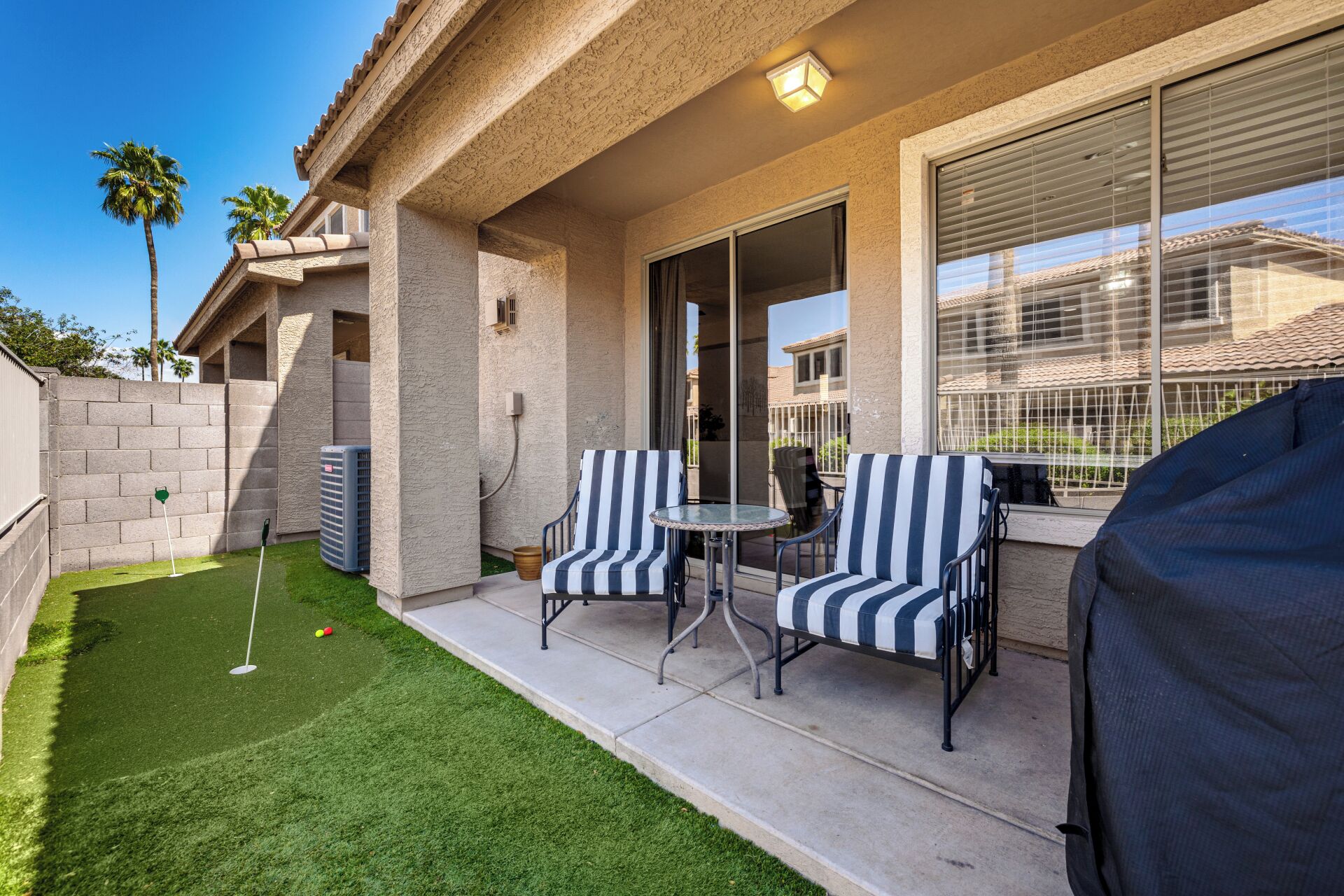 A patio with two striped chairs, a small table, and a grill.