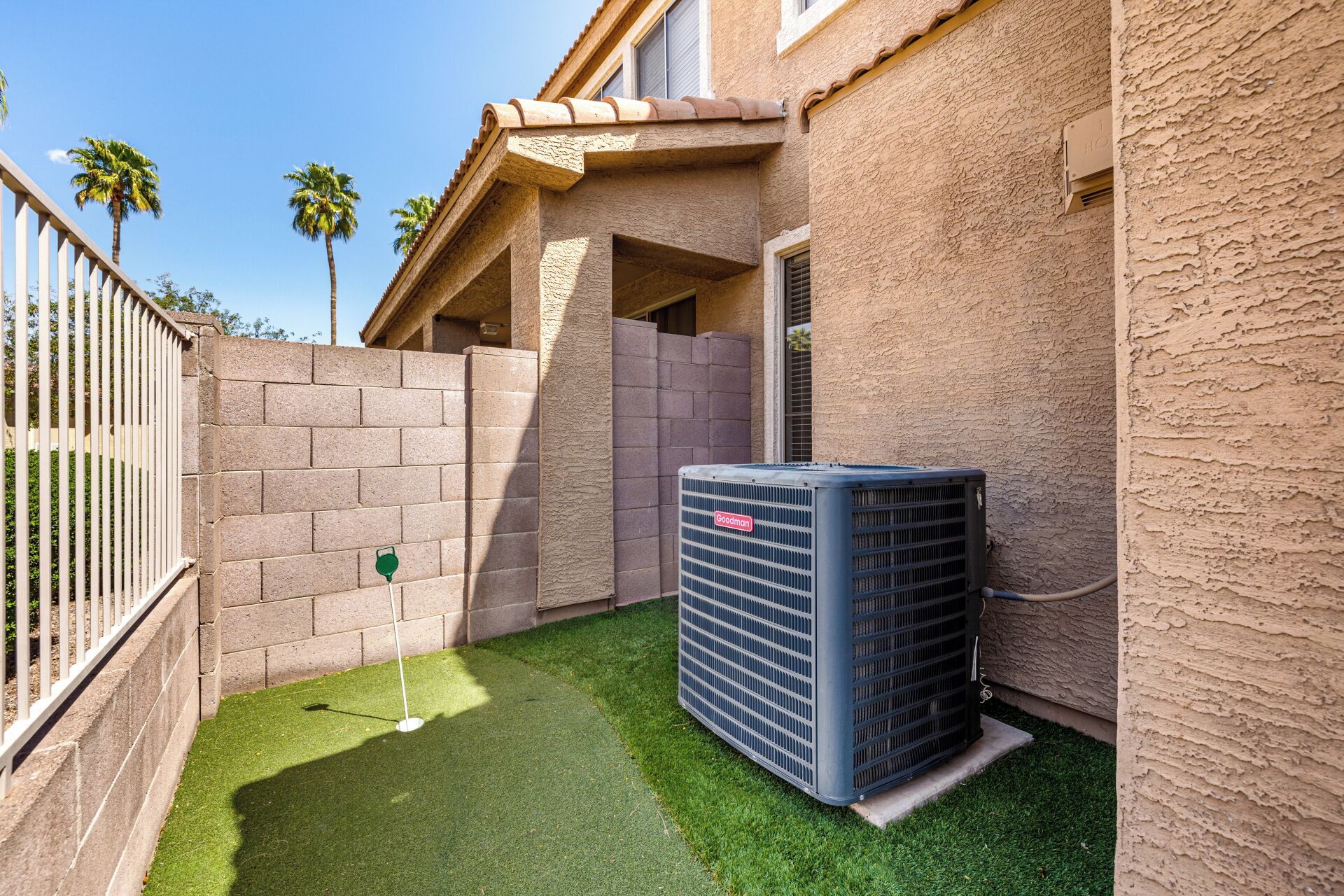 Zona residenziale con un muro in mattoni, un piccolo patio con erba sintetica e un condizionatore d'aria di grandi dimensioni.