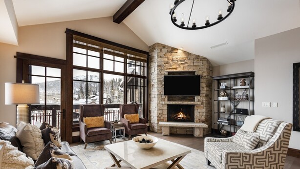 A cozy living room with a stone fireplace, comfortable seating, and a large window offering a view of the outdoors. - Luxury Ski-In, Ski-Out Arrowleaf Penthouse  With Panoramic Views (Park City)