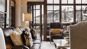 A cozy living room with a leather sofa, a wooden coffee table, and a view of snowy mountains through large windows. - Luxury Ski-In, Ski-Out Arrowleaf Penthouse  With Panoramic Views (Park City)
