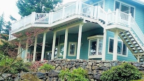 A two-story house with a stone foundation, a porch with white railings, and a staircase leading to the upper level. - Movie Theater! Hot Tub! Private Rental 3 Bedrooms and 2 Bathrooms. (Bellingham)