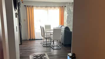 A modern living room with a dining area, a patterned rug, and a view of the outdoors through large windows.