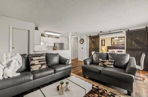 A modern living room with two leather sofas, a coffee table, and a kitchen in the background.