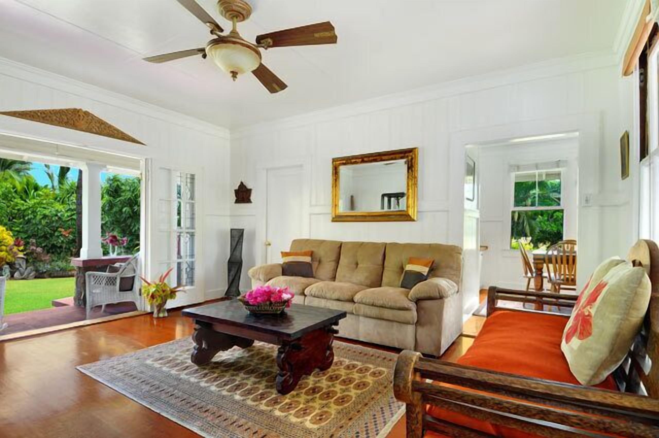 A spacious living room with a ceiling fan, a sofa, a coffee table with flowers, and a view of the outdoors.