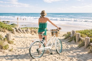 A person on a beach with a bicycle, a wooden fence, and the ocean in the background. - Beach Cottage + Bikes + Walk to Dining & Sunsets. (Indian Rocks Beach)