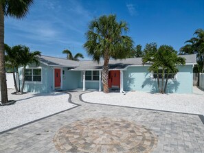 A two-story house with a red door, a covered porch, and a paved driveway with a circular pattern. - Hidden Beach Gem - Walk to Beach, Dining & Sunset Views! (Indian Rocks Beach)