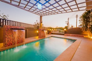 Ein Schwimmbecken mit Mosaikfliesen und einer überdachten Pergola.