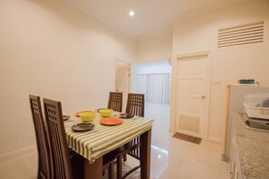 Un coin repas avec une table dressée pour quatre personnes, des chaises et un espace cuisine comprenant un réfrigérateur et un évier.