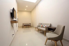 Un salon moderne avec un téléviseur à écran plat fixé au mur, un banc et deux canapés agrémentés de coussins à motifs.