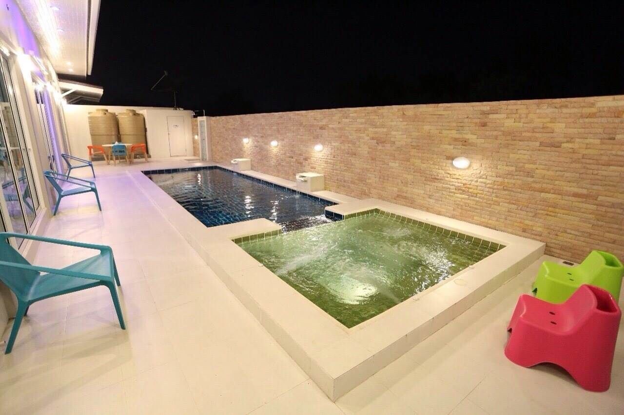 A swimming pool area with a jacuzzi, outdoor seating, and a brick wall.