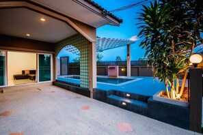 A modern outdoor area with a pool, steps leading to a covered patio, and a large plant.