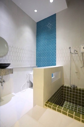 A bathroom with a white sink, a mirror, a toilet, a shower area, and a bathtub with green tiles.