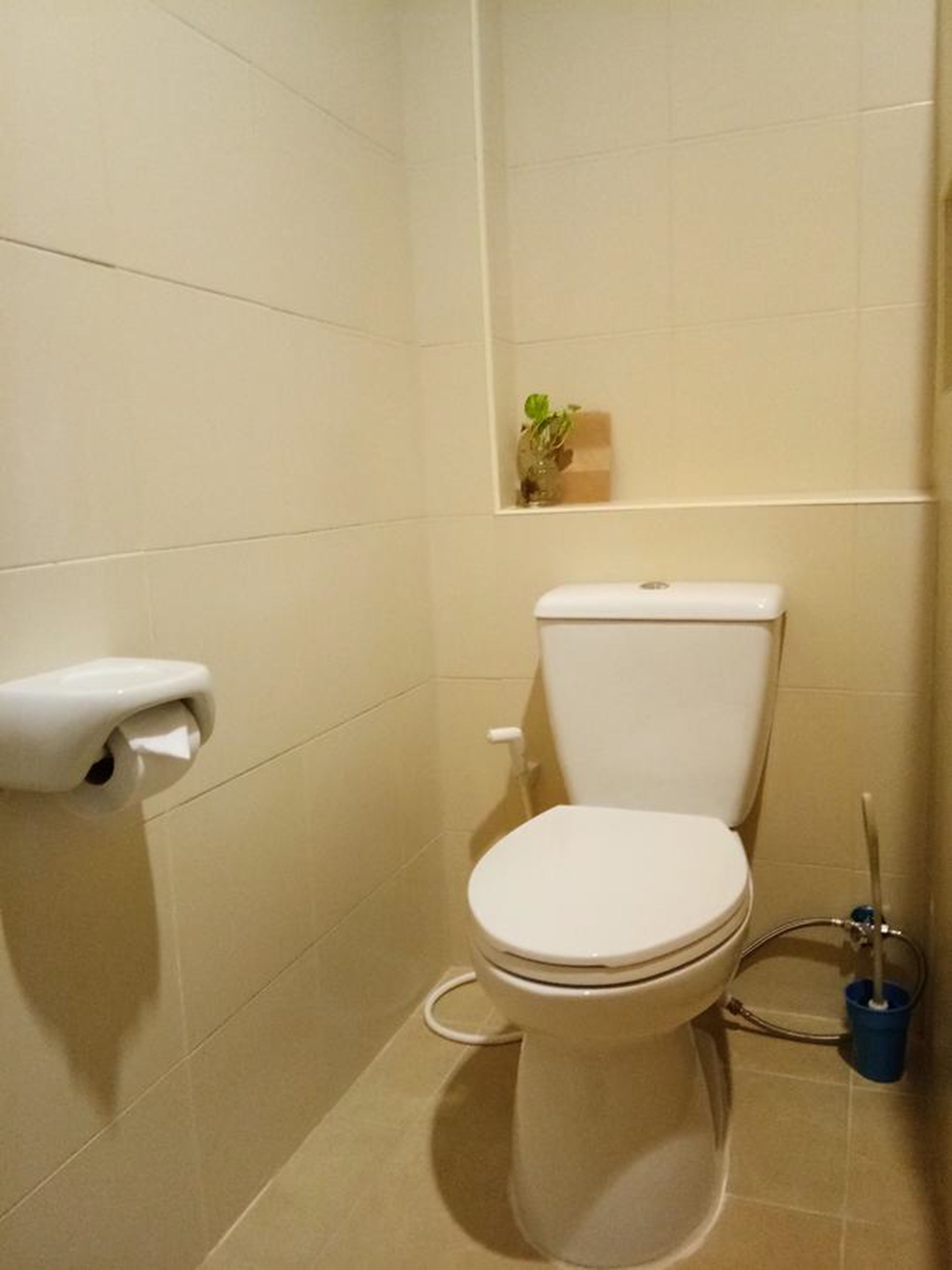 Une petite salle de bain propre, équipée de toilettes, d’un porte-rouleau de papier toilette et d’un seau de nettoyage bleu.