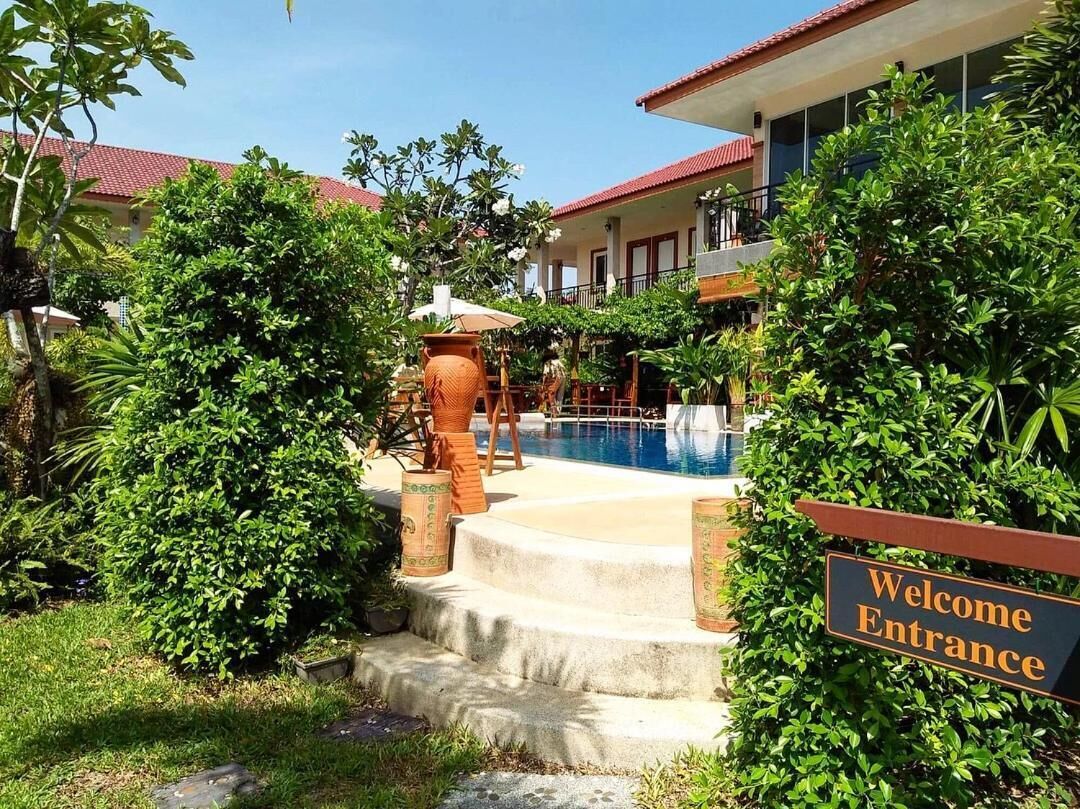 A pool area with steps leading to a building, surrounded by lush greenery. A sign reads "Welcome Entrance."