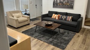 Ein Wohnzimmer mit einem beigen Sessel, einem dunklen Sofa, einem Couchtisch und einem Stadtbild an der Wand.