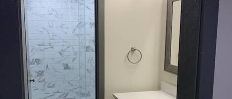 A narrow hallway leading to a bathroom with a glass shower door, a white sink, and a mirror.
