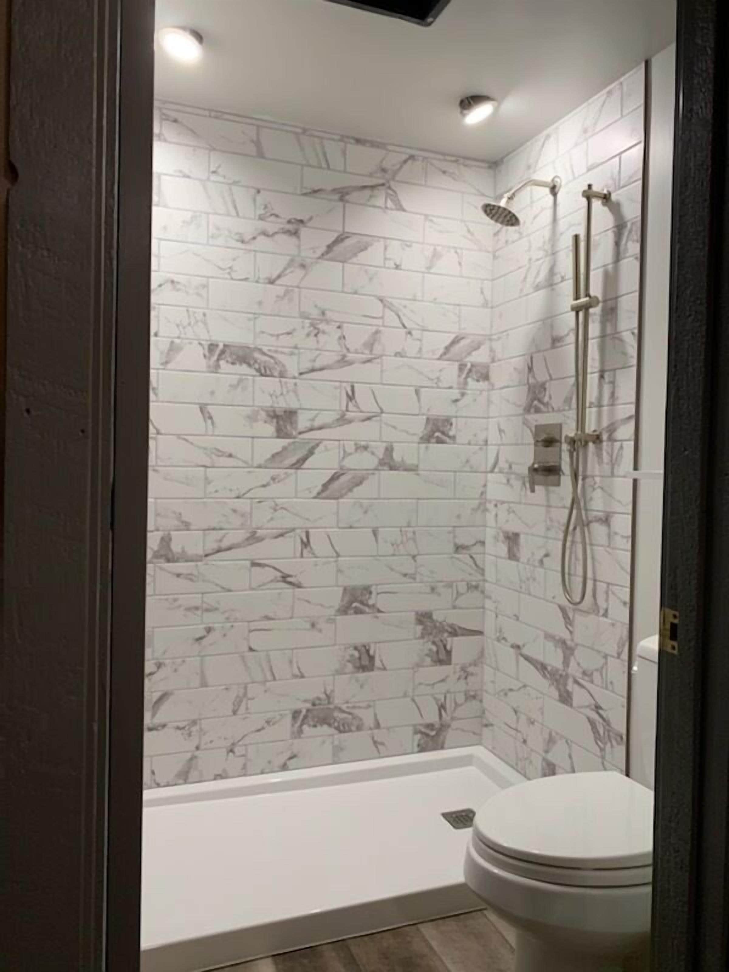 A bathroom with a shower, toilet, and marble-patterned walls.