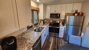 Cocina compacta con armarios blancos, un refrigerador de acero inoxidable, un microondas, una estufa y una cafetera.