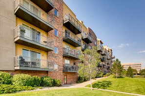 A multi-story residential building with balconies, a brick facade, and a well-maintained lawn.